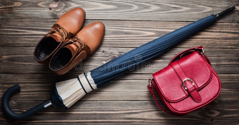 Demi-season leather half-boots, a red bag and a folded umbrella on a wooden floor. Top view. Waxing women& x27;s accessories for rainy weather.