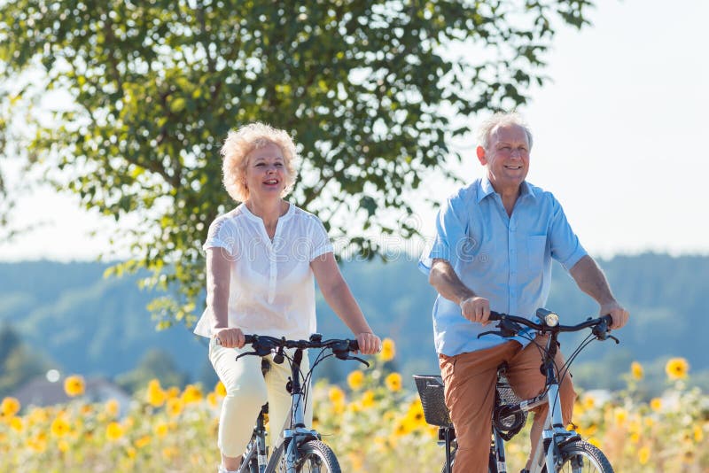 Active elderly couple wearing summer casual clothes while riding bicycles together in the countryside. Active elderly couple wearing summer casual clothes while riding bicycles together in the countryside