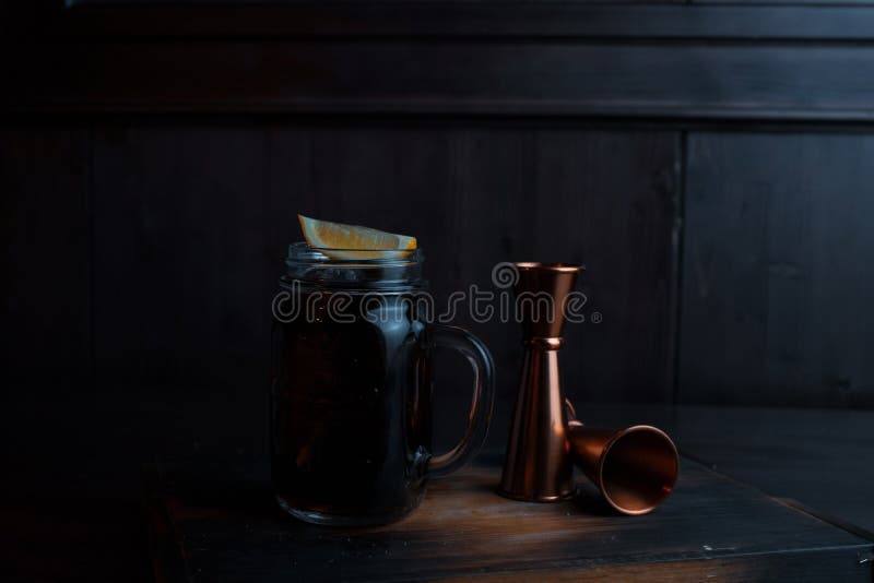 Den alkoholiserade coctailen med is, whisky och coca-cola, citronskivor står på en trätabell i en restaurang bredvid metall royaltyfri foto Den alkoholiserade coctailen med is, whisky och coca-cola, citronskivor står på en trätabell i en restaurang bredvid metall royaltyfri foto