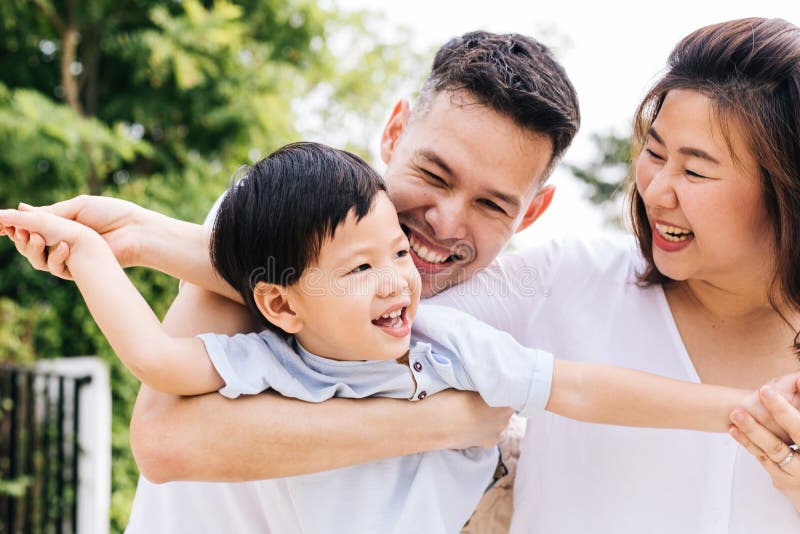 Den asiatiska familjen som har roligt och bär ett barn parkerar offentligt arkivfoton Den asiatiska familjen som har roligt och bär ett barn parkerar offentligt arkivfoton