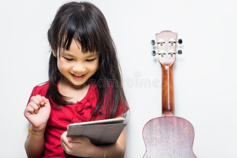 Den asiatiska flickan använder hennes minnestavla för att lära att spela musik royaltyfri fotografi Den asiatiska flickan använder hennes minnestavla för att lära att spela musik royaltyfri fotografi