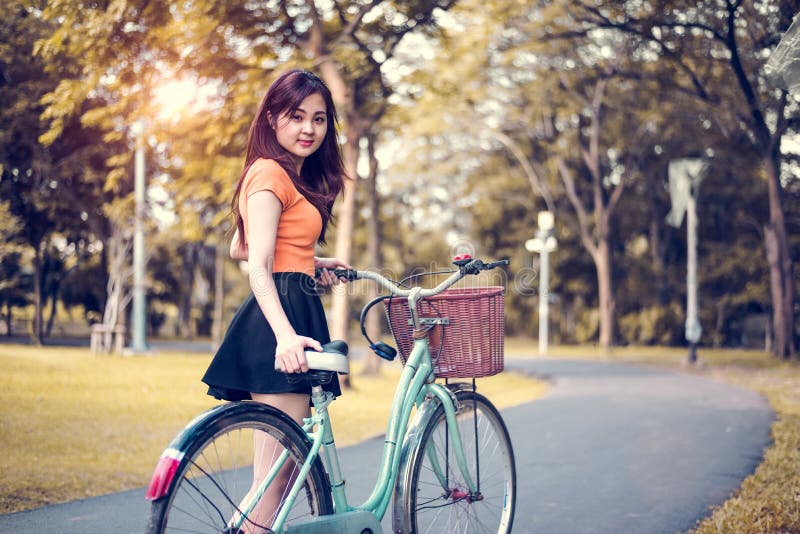Den asiatiska kvinnaståenden parkerar offentligt med cykeln Folk och livsstilbegrepp Avkoppling- och aktivitetstema arkivfoto Den asiatiska kvinnaståenden parkerar offentligt med cykeln Folk och livsstilbegrepp Avkoppling- och aktivitetstema arkivfoto