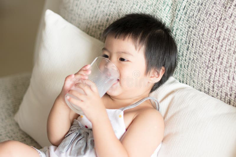 Den asiatiska lilla gulliga flickan är rymma, och dricka ett exponeringsglas av mjölka I arkivfoto Den asiatiska lilla gulliga flickan är rymma, och dricka ett exponeringsglas av mjölka I arkivfoto