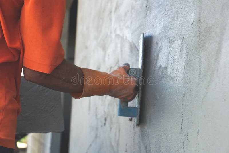 Den asiatiska manliga hus-byggmästaren handen som bär den orange handsken som slätar morteln, applicerade på en utomhus- vägg royaltyfria bilder Den asiatiska manliga hus-byggmästaren handen som bär den orange handsken som slätar morteln, applicerade på en utomhus- vägg royaltyfria bilder
