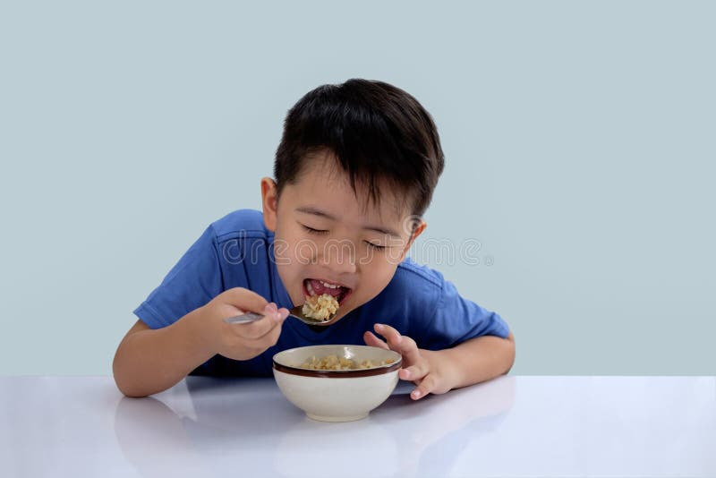 Den asiatiska pojken äter läckra ris och har en jätteglad framsida arkivfoto