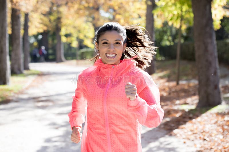 Den attraktiva och lyckliga löparekvinnan i höstsportswearspring och utbildning på att jogga utomhus genomkörare i stad parkerar