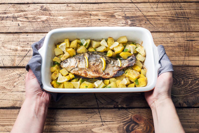 Den bakade fisken kverulerar med potatisar i en keramisk panna Lantlig stil arkivfoton Den bakade fisken kverulerar med potatisar i en keramisk panna Lantlig stil arkivfoton