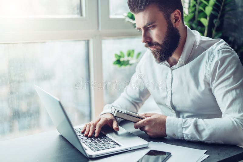 Den barn uppsökte affärsmannen i den vita skjortan sitter på tabellen och arbete på bärbara datorn Freelanceren arbetar hemma Stu arkivbild Den barn uppsökte affärsmannen i den vita skjortan sitter på tabellen och arbete på bärbara datorn Freelanceren arbetar hemma Stu arkivbild