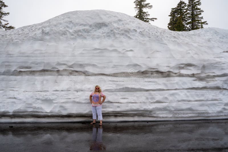 Den blonda turisten stÃ¥r bredvid en stor massa plöjd snö i Lassen National Park California under sommaren royaltyfria foton Den blonda turisten stÃ¥r bredvid en stor massa plöjd snö i Lassen National Park California under sommaren royaltyfria foton