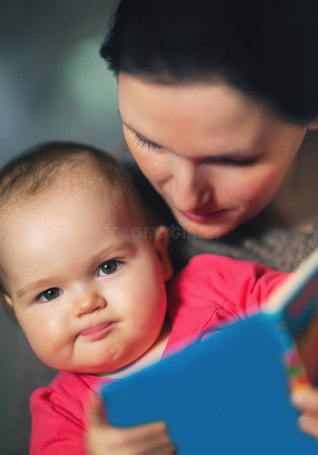 Den charmiga modervisningen avbildar i en bok till hennes gulliga litet behandla som ett barn royaltyfri bild Den charmiga modervisningen avbildar i en bok till hennes gulliga litet behandla som ett barn royaltyfri bild