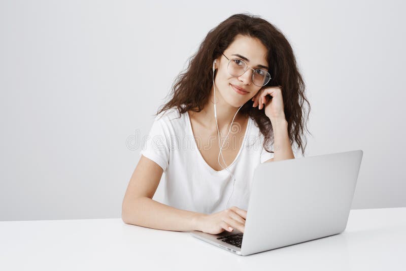 Den charmiga redaktören tycker om att arbeta i hemtrevlig atmosfär Studion sköt av snyggt lockig-haired kvinnligt arbete på bärba fotografering för bildbyråer Den charmiga redaktören tycker om att arbeta i hemtrevlig atmosfär Studion sköt av snyggt lockig-haired kvinnligt arbete på bärba fotografering för bildbyråer
