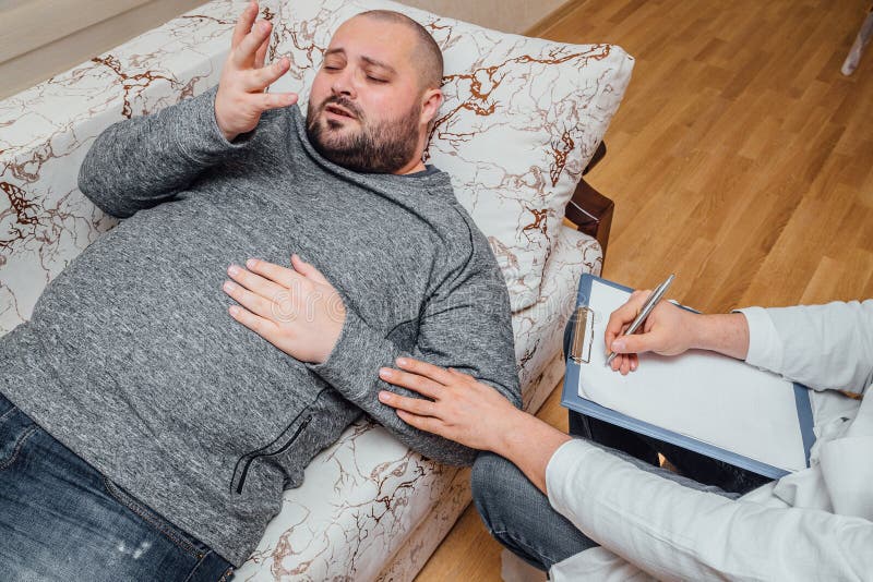 Den deprimerande mannen besöker en psykolog Psychologist som skriver anmärkningar och, uppmuntrar hans patient fotografering för bildbyråer Den deprimerande mannen besöker en psykolog Psychologist som skriver anmärkningar och, uppmuntrar hans patient fotografering för bildbyråer