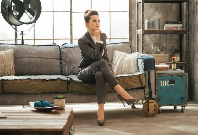 Den eleganta brunettaffärskvinnan sitter på soffan i vind royaltyfri bild Den eleganta brunettaffärskvinnan sitter på soffan i vind royaltyfri bild