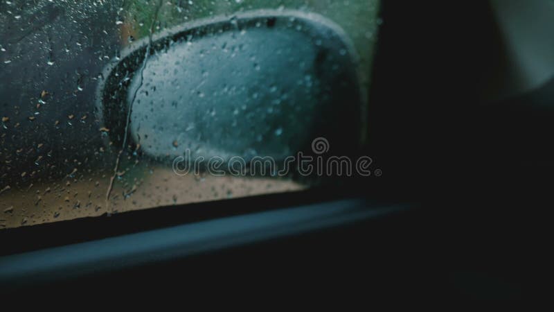 Den filmiska nÃ¤rbilden, den defocused spegeln fÃ¶r sidosikten ses frÃ¥n inre den rÃ¶rande bilen, fokus pÃ¥ regndroppar pÃ¥ fÃ¶ns