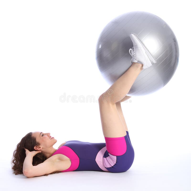 Fit beautiful brunette woman with big smile lying on the floor lifting exercise ball using her legs as part of workout routine. She is wearing bright blue and pink sports clothes and white trainers. Fit beautiful brunette woman with big smile lying on the floor lifting exercise ball using her legs as part of workout routine. She is wearing bright blue and pink sports clothes and white trainers.