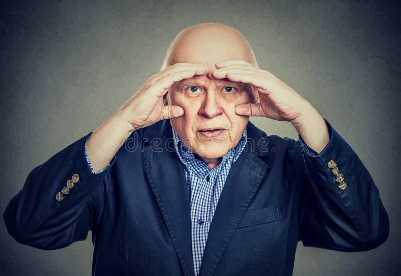 Den förargade äldre mannen som ser till och med händer som kikare, har visionproblem royaltyfri fotografi Den förargade äldre mannen som ser till och med händer som kikare, har visionproblem royaltyfri fotografi