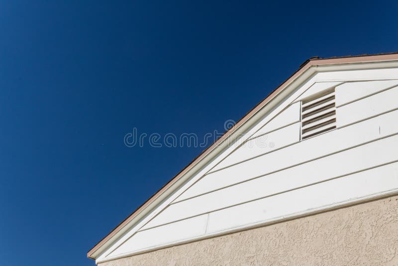 Generic house view of side and roof edge, stucco and vinyl with attic ventilation set against a deep blue sky, copy space, horizontal aspect. Generic house view of side and roof edge, stucco and vinyl with attic ventilation set against a deep blue sky, copy space, horizontal aspect