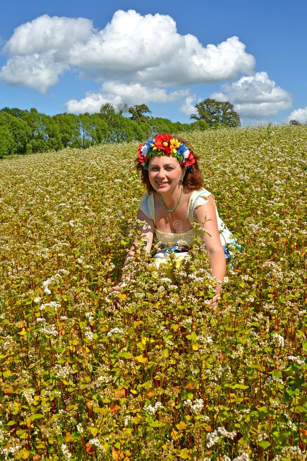 Den glade kvinnan av genomsnittliga år med en krans på huvudet i te som blomstrar bovetefältet arkivbilder Den glade kvinnan av genomsnittliga år med en krans på huvudet i te som blomstrar bovetefältet arkivbilder
