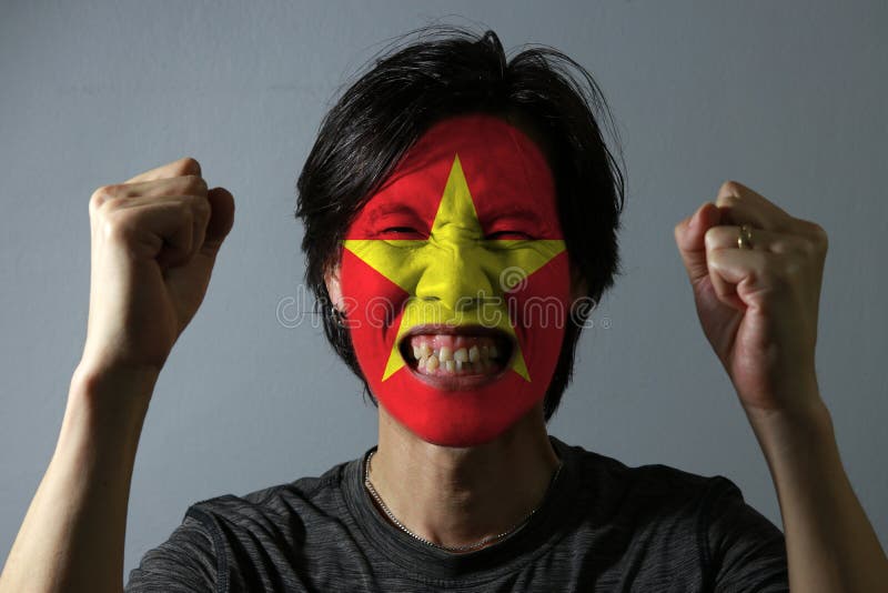 Den gladlynta ståenden av en man med flaggan av Vietnam målade på hans framsida på grå bakgrund Begreppet av sporten eller nation royaltyfri fotografi Den gladlynta ståenden av en man med flaggan av Vietnam målade på hans framsida på grå bakgrund Begreppet av sporten eller nation royaltyfri fotografi