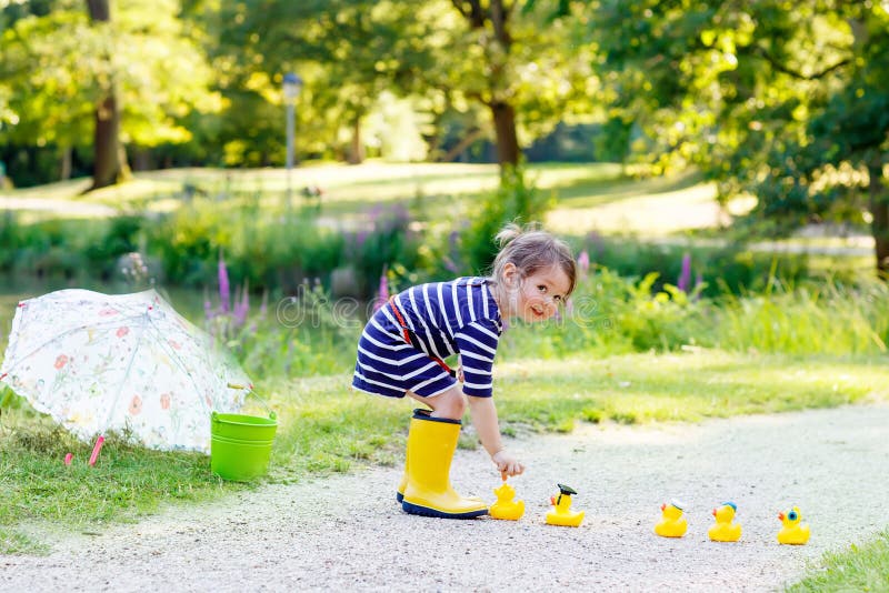 Den gulliga flickan för den lilla ungen i gula rainboots i sommar parkerar fotografering för bildbyråer Den gulliga flickan för den lilla ungen i gula rainboots i sommar parkerar fotografering för bildbyråer