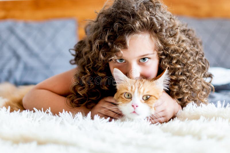 Den gulliga flickan med lockigt h? r kramar en r? d katt fotografering för bildbyråer