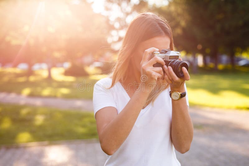 Den gulliga flickan på solig dag i parkering som tar foto med motsvarighet, kom royaltyfri bild Den gulliga flickan på solig dag i parkering som tar foto med motsvarighet, kom royaltyfri bild