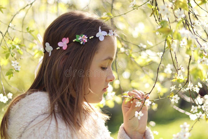 Den gulliga lilla eftertänksamma flickan med den handgjorda hårkransen på hennes huvud som luktar blommor blomstrar på våren, trä arkivbilder Den gulliga lilla eftertänksamma flickan med den handgjorda hårkransen på hennes huvud som luktar blommor blomstrar på våren, trä arkivbilder
