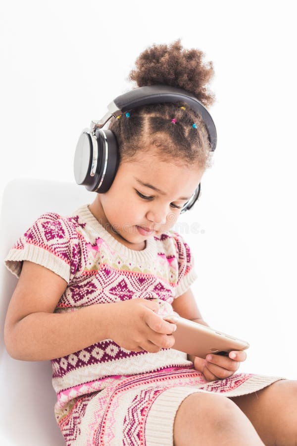 Den gulliga lilla flickan i enfärgad klänning, lyssnar till musik med hörlurar och använder en smartphone på en vit bakgrund fotografering för bildbyråer Den gulliga lilla flickan i enfärgad klänning, lyssnar till musik med hörlurar och använder en smartphone på en vit bakgrund fotografering för bildbyråer