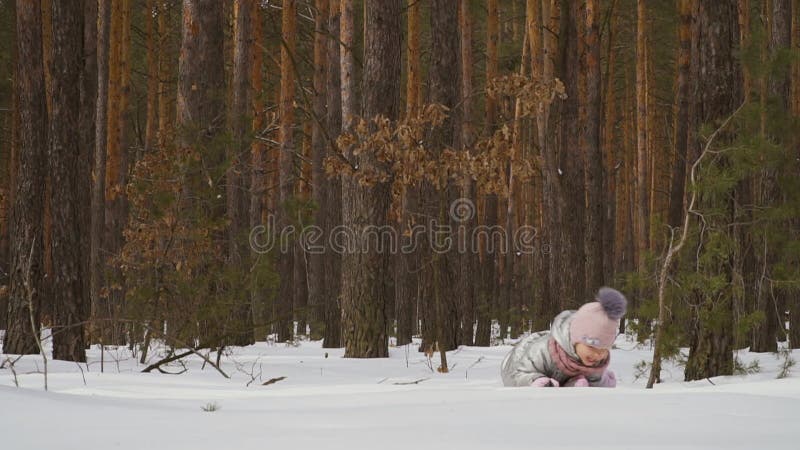 Den gulliga lilla flickan kryper på den insnöade vinterskogen