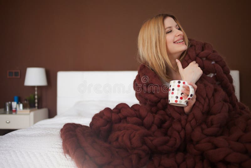 Den gulliga unga kvinnan sitter på sängen som slås in i en stor och fluffig brun pläd Härlig flicka i en hemtrevlig filt royaltyfri bild Den gulliga unga kvinnan sitter på sängen som slås in i en stor och fluffig brun pläd Härlig flicka i en hemtrevlig filt royaltyfri bild