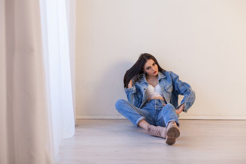 Beautiful girl in jeans clothes sitting on the floor in a white room 1. Beautiful girl in jeans clothes sitting on the floor in a white room 1