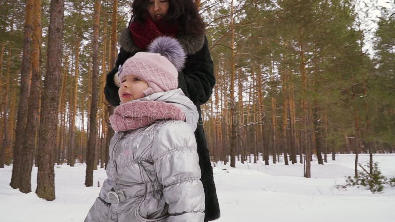Den härliga kvinnan går i vinterskog med den lilla dottern