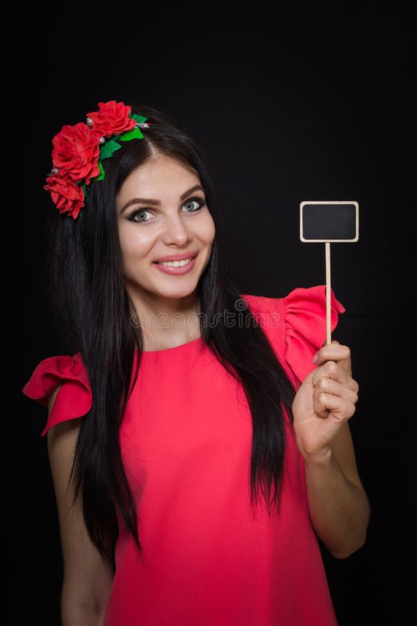 Den härliga kvinnan med en krans av röda blommor rymmer en träplatta royaltyfria foton Den härliga kvinnan med en krans av röda blommor rymmer en träplatta royaltyfria foton