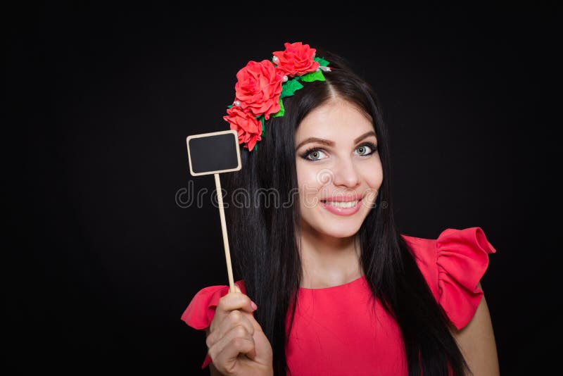 Den härliga kvinnan med en krans av röda blommor rymmer en träplatta royaltyfri fotografi Den härliga kvinnan med en krans av röda blommor rymmer en träplatta royaltyfri fotografi