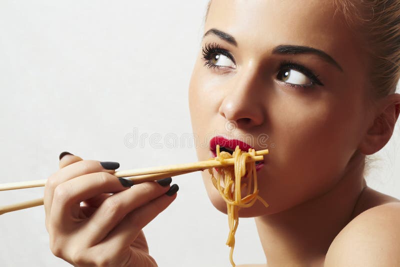Den härliga kvinnan äter noodles.red-kanter. Kinespinnar. snabbmat royaltyfri foto Den härliga kvinnan äter noodles.red-kanter. Kinespinnar. snabbmat royaltyfri foto