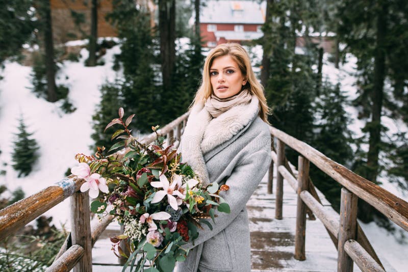 Den härliga unga flickan står i vinter med en bukett av blommor i hennes händer arkivbild Den härliga unga flickan står i vinter med en bukett av blommor i hennes händer arkivbild