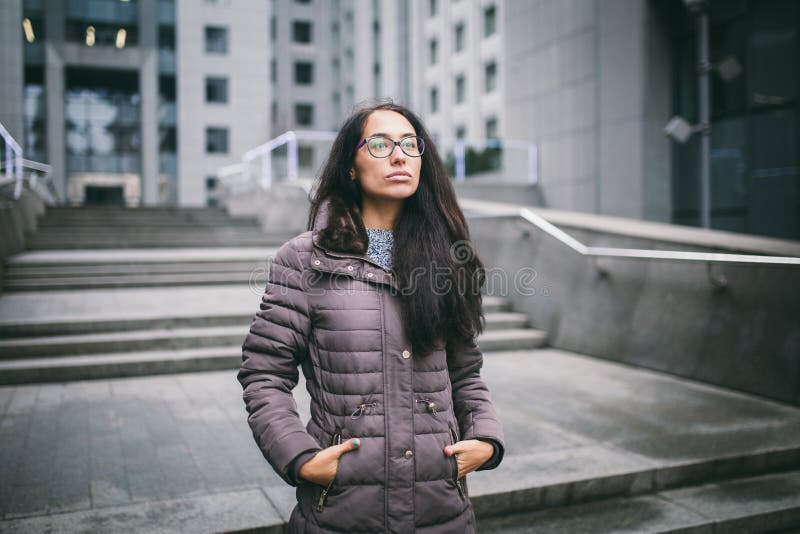 Den härliga unga kvinnan av europeisk etnicitet med långt brunetthår, bärande exponeringsglas och ett lag står mot bakgrunden av arkivfoto