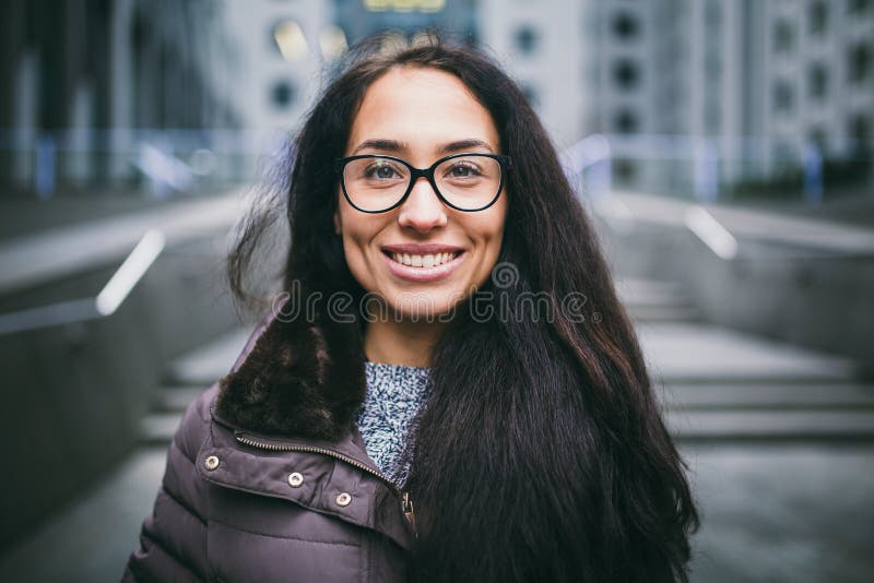 Den härliga unga kvinnan av europeisk etnicitet med långt brunetthår med ett toothy leende-, bäraexponeringsglas och lag står mot royaltyfri foto