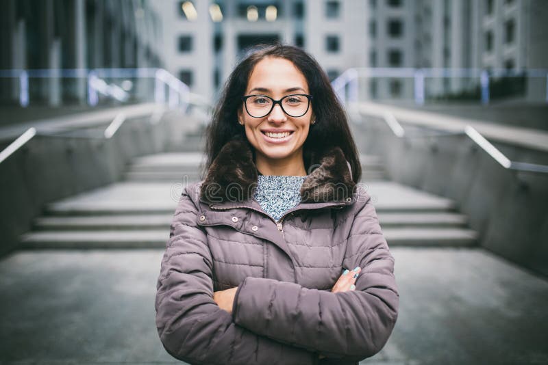 Den härliga unga kvinnan av europeisk etnicitet med långt brunetthår med ett toothy leende-, bäraexponeringsglas och lag står mot royaltyfri foto