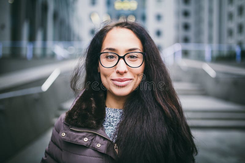 Den härliga unga kvinnan av europeisk etnicitet med långt brunetthår med ett toothy leende-, bäraexponeringsglas och lag står mot royaltyfri bild