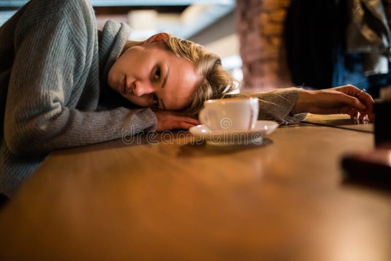 Den härliga unga kvinnan ligger på händer, sitter på trätabellen i kafeteria, dricker kaffe Koppla av och vila begreppet royaltyfria bilder Den härliga unga kvinnan ligger på händer, sitter på trätabellen i kafeteria, dricker kaffe Koppla av och vila begreppet royaltyfria bilder