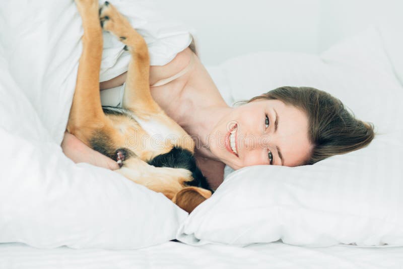 Den härliga upphetsade kvinnan och hennes gulliga byrackahund är bedrar omkring och att se kameran, medan att ligga som täckas me arkivfoton Den härliga upphetsade kvinnan och hennes gulliga byrackahund är bedrar omkring och att se kameran, medan att ligga som täckas me arkivfoton
