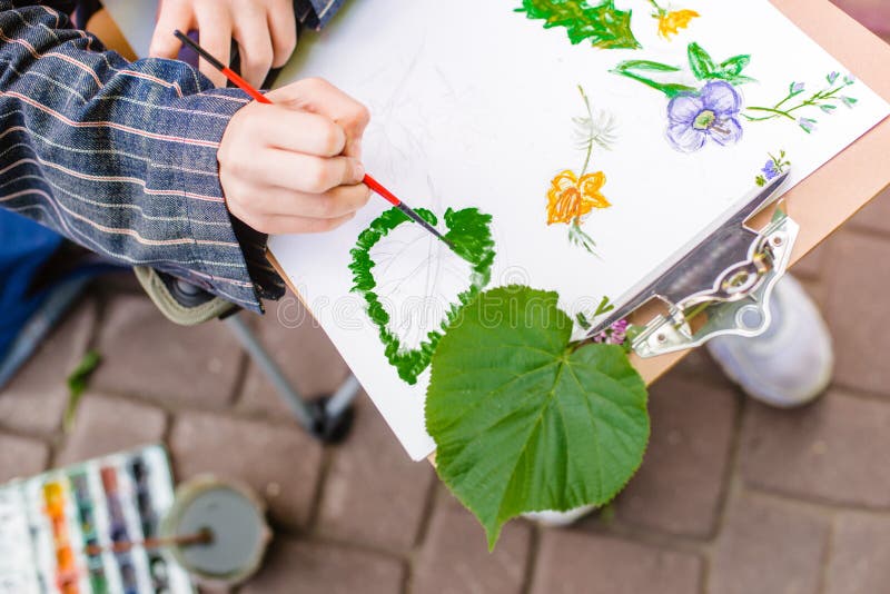 Den idérika konstnären målar en färgrik bild Närbild av händer och borsten i processen av målning utomhus arkivbild Den idérika konstnären målar en färgrik bild Närbild av händer och borsten i processen av målning utomhus arkivbild