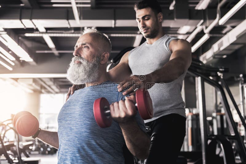 Den koncentrerade höga mannen utbildar hans biceps i idrottshall royaltyfria bilder Den koncentrerade höga mannen utbildar hans biceps i idrottshall royaltyfria bilder