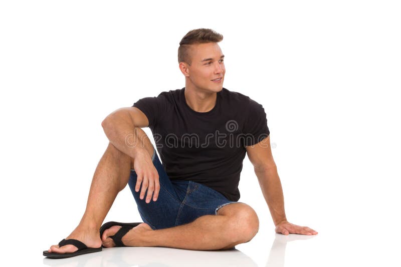Den kopplade av mannen sitter på ett golv och ser bort royaltyfri bild Den kopplade av mannen sitter på ett golv och ser bort royaltyfri bild