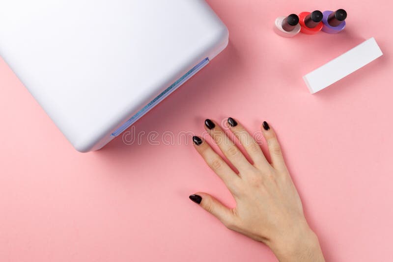 Den kvinnliga handen med manFemalehanden med manicured spikar och UV lampan royaltyfria bilder Den kvinnliga handen med manFemalehanden med manicured spikar och UV lampan royaltyfria bilder