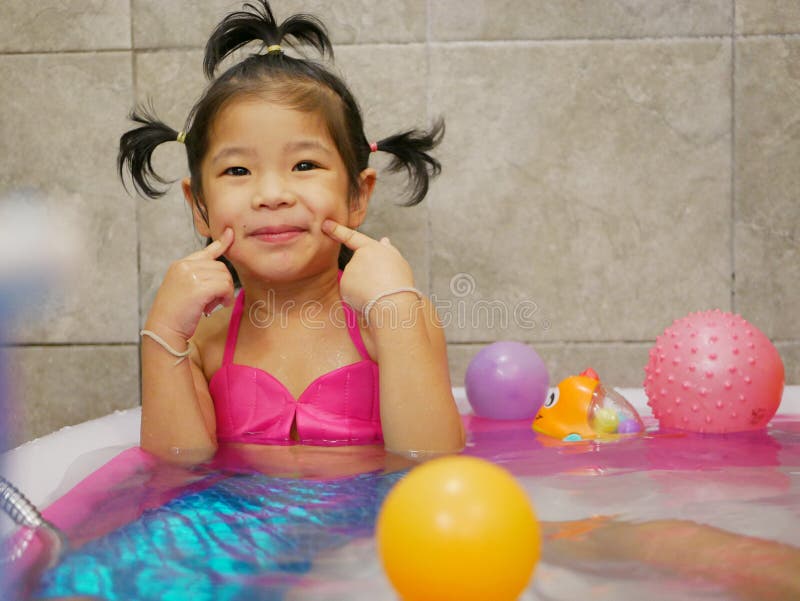 Den lilla asiatiska flickan tycker om att bli klädd som en barmman och spela vatten i en liten pool hemma royaltyfria bilder
