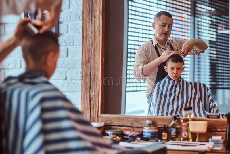 Den lilla charmiga pojken f?r moderiktig frisyr fr?n mogen fris?r p? den trendiga friseringsalongen royaltyfri fotografi Den lilla charmiga pojken f?r moderiktig frisyr fr?n mogen fris?r p? den trendiga friseringsalongen royaltyfri fotografi