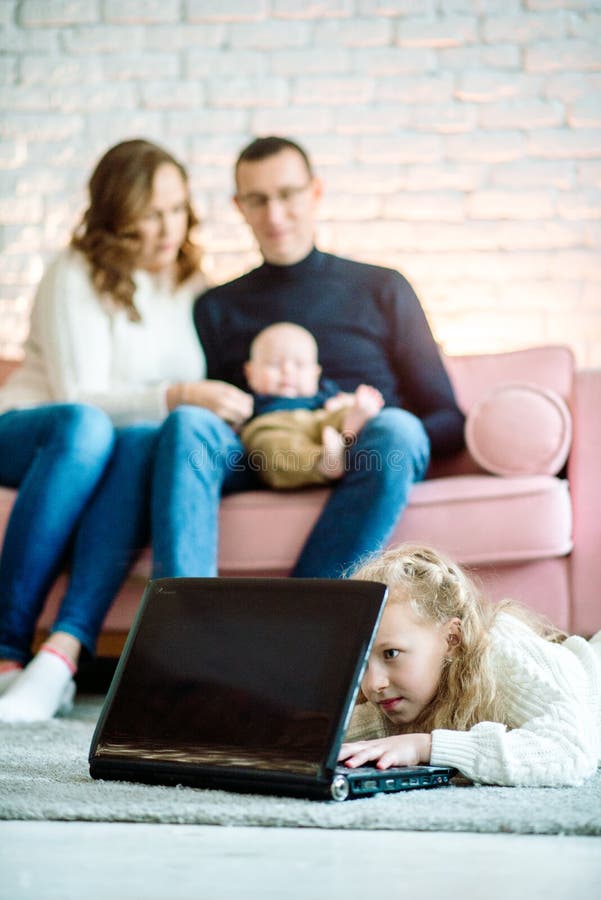Den lilla flickan i Cute använder en digital tablett när hon ligger på golvet hemma, i bakgrunden sin stiliga far och mor med arkivfoton