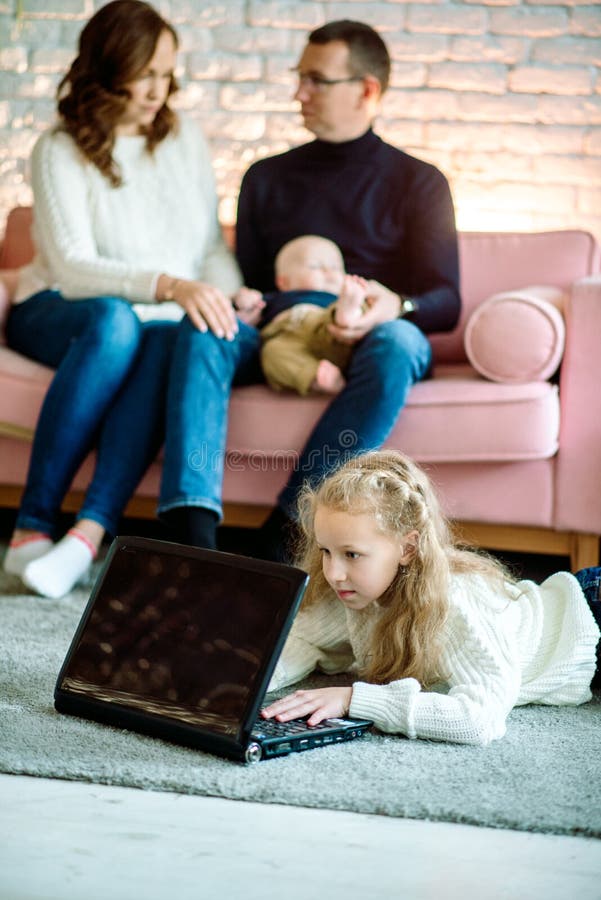 Den lilla flickan i Cute använder en digital tablett när hon ligger på golvet hemma, i bakgrunden sin stiliga far och mor med arkivfoto